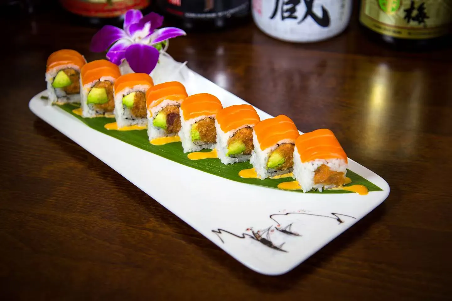 Salmon topped fried filling sushi roll laid on green banana leaf at Midori Sushi Of Highland Park, a Japanese Restaurant in Highland Park
