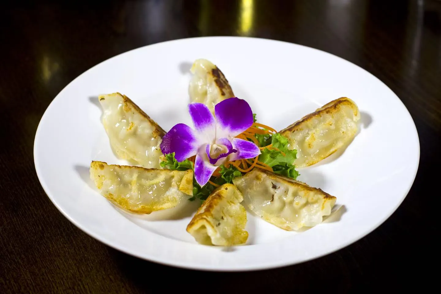 Golden pan-fried gyoza dumplings garnished with purple orchid and shredded veggies at Midori Sushi Of Highland Park, a Japanese Restaurant in Highland Park